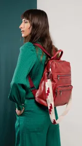 Mochila negra de símil cuero con apertura superior y tres bolsillos frontales con cierres metálicos. Incluye bolsillos laterales y tres bolsillos internos. Tiene correa larga de galón regulable para usar como bandolera y correas para colgar en la espalda.