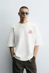 Sudadera blanca de cuello redondo y manga corta, corte relaxed boxy fit, con estampado en el frente y la espalda.