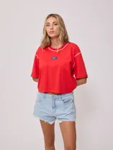 Remera gris de algodón con corte cropped y calce holgado. Tiene cuello redondo y mangas cortas con costuras reforzadas en color coral. Presenta un pequeño logo de la marca Rusty en el pecho.