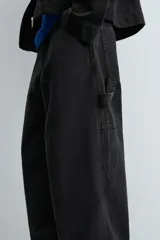 Pantalón negro de corte amplio, confeccionado en tejido de algodón con efecto lavado. Presenta bolsillos frontales, traseros de parche, tira multifunción y bolsillos laterales en las perneras. Cuenta con cierre frontal con cremallera y botón.