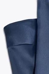 Top azul de satén con escote recto y hombros descubiertos. Tiene detalle de bufanda en el cuello y cierre lateral con cremallera oculta.