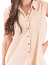 Mono corto color beige, con cuello camisero, sin mangas y cierre frontal con botones.