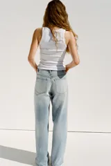 Pantalón de jean celeste de tiro alto, corte wide leg y largo hasta el tobillo. Presenta un diseño asimétrico en la cintura con cierre frontal cruzado con cremallera y botones metálicos.