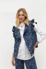 Chaleco de denim azul con volados en hombros y frente, cierre con botones metálicos y bolsillos laterales.