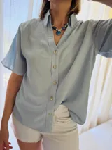 Camisa celeste de lino con mangas cortas, botones de lino y detalle drapeado en la espalda.