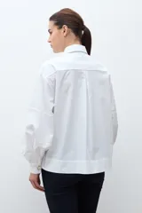Camisa blanca de manga larga con puños fruncidos y cuello abotonado, corte holgado.