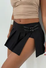 Short pollera tableada negro con tajo lateral y hebillas decorativas.