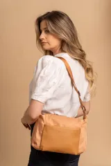 Bandolera de diseño moderno, color beige rosado, con correa regulable y bolsillo frontal con cierre.