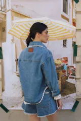 Campera de jean celeste con cuello camisero, cierre frontal con botones metálicos, bolsillos de parche en el pecho con solapa y detalle de puntilla blanca en cuello, solapas, bolsillos y ruedo.