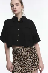 Camisa corta negra con cuello clásico, cierre frontal con botones, mangas cortas con dobladillo y dos bolsillos de parche en el pecho.