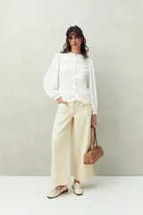 Camisa color marrón claro con cuello mao, mangas 3/4 abullonadas y cierre frontal con botones. Presenta pequeños pliegues en los hombros y detalle calado sutil.