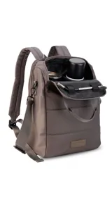 Mochila matera confeccionada en tela impermeable color marrón, diseñada con dos compartimientos independientes: uno para el kit de mate y otro para objetos personales. Cuenta con correas de mochila acolchadas, asa de mano superior y una correa de hombro ajustable y extraíble. El diseño presenta costuras horizontales acolchadas y un parche frontal con el logo de la marca.