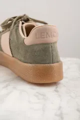 Zapatilla deportiva de cuero color verde oliva con detalles en rosa y suela marrón.