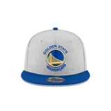Gorra gris con visera azul, logo de los Golden State Warriors bordado en el frente y logo de New Era bordado en el lateral.