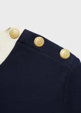Camiseta azul marino de manga corta con cuello redondo y ribete blanco en cuello y mangas. Presenta botones decorativos dorados en el hombro.