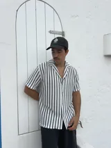 Camisa tejida a rayas verticales blancas y negras, de manga corta y cuello solapa.