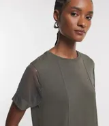 Blusa de color verde militar con cuello redondo y mangas cortas de tul. El cuerpo de la blusa es de media malla con costuras verticales visibles.