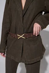 Cinturón negro de cuero con tachas plateadas y hebilla metálica en forma de X.