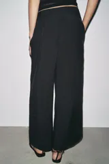 Pantalón cropped marrón de tiro medio y pierna ancha, confeccionado en hilatura con mezcla de lyocell. Presenta trabillas en la cintura, bolsillos laterales y pinzas en el delantero. Cierre frontal con cremallera y botón.