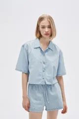 Camisa celeste de jean, corte cropped, con cuello camisero, cierre frontal con botones y mangas cortas.