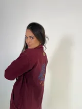 Tapado largo de jeans color bordó con cuello camisero, cierre frontal con botones a presión, mangas largas con puños abotonados, bolsillos laterales y bordado floral en la espalda.