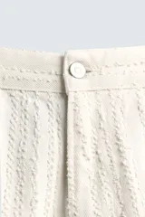 Pantalón de jean color crudo con textura de rayas verticales, corte relaxed fit, tiro medio, cinco bolsillos y cierre frontal con cremallera y botón.