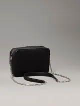 Bandolera negra con monograma CK grabado en toda la superficie. Tiene correa de cadena plateada, cierre superior con cremallera, bolsillo frontal con cierre giratorio y herrajes plateados.