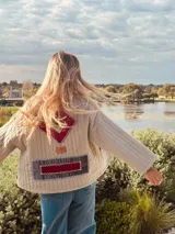 Campera capitoneada color beige con figuras geométricas bordadas a mano en terciopelo color borgoña y gris. Tiene cuello redondo, mangas largas y bolsillos al frente.