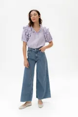 Camisa de lino color lila con volados en el cuello y en las mangas cortas abullonadas. Presenta un diseño de corte recto con cierre frontal de botones.