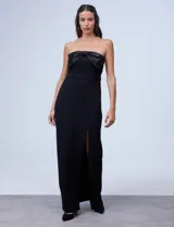 Vestido de fiesta corto strapless, color negro, confeccionado en crepe. Presenta escote recto con aplique de moño en satén y tajo en la parte delantera.