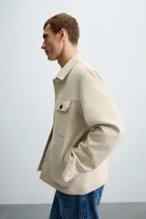 Sobrecamisa color beige de tejido efecto ante, corte regular fit, con cuello solapa, manga larga con puños abotonados, bolsillos de parche con solapa en el pecho y bolsillos de ojal en la cadera.