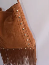 Bolso tipo bandolera de cuero negro con flecos y tachas plateadas. Tiene correa regulable, forro interior y bolsillo interno.