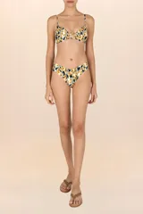 Top de bikini tipo triángulo con estampado de hojas en tonos mostaza, negro y blanco. Presenta tirantes delgados ajustables y un accesorio metálico dorado con forma de hoja en el centro del busto.