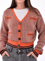 Cárdigan tejido con patrón geométrico en tonos naranja, negro y blanco. Tiene cuello en V, cierre con botones negros y ribetes a contraste en cuello, puños y bajo.