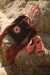 Conjunto de bolso tipo tote y sandalias de gamuza color coral. El bolso es negro con un estampado de sol en color coral y flecos largos. Las sandalias son abiertas con detalles de costuras en color blanco.