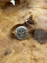 Pulsera dorada con dije circular con la figura del Espíritu Santo y banda de terciopelo verde.