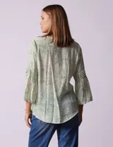 Blusa de gasa estampada color salmón con flores blancas, marca Ruby Rd. Cuello a la base, escote en V y abertura central con botones. Delantera con plisados. Largo de manga ¾ con terminación amplia.