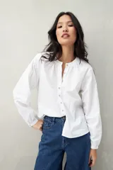 Camisa blanca de algodón con cuello mao con leve frunce, abotonadura frontal con botones de nácar y mangas amplias con puños fruncidos.