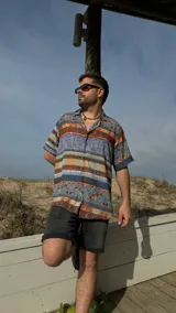 Camisa manga corta con cuello, de corte amplio y estampado con motivos geométricos y florales en tonos azul, marrón, naranja y beige.