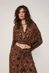 Camisa marrón con estampado geométrico de rombos negros, cuello alto, manga larga, cierre de botones, canesú con sisa descentrada y corte fruncido.