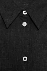 Camisa amplia color negro confeccionada con hilatura de lino. Tiene cuello solapa, manga larga, bolsillo de plastrón en el delantero, bajo asimétrico y cierre frontal con botones.