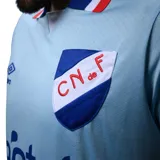 Camiseta de fútbol Puma del Club Nacional de Football, modelo Away 3 2024. Diseño celeste con detalles en rojo y blanco en cuello y mangas. Incluye logo de Puma, escudo del club y sponsor Antel en el frente.