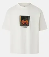 Remera de corte boxy color crudo, con cuello redondo y mangas cortas. Estampa frontal con dibujo de perros jugando a las cartas y texto 'underappreciated crew 1989-90'.