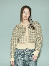 Cardigan de punto color crema con diseño geométrico en negro y verde, cuello redondo, cierre frontal con botones y ribete acanalado en puños y bajo.