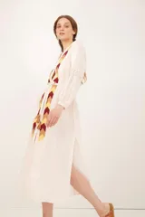 Saco color crema con bordado de flechas en tonos amarillo, marrón y rojo. Tiene mangas largas con detalle de puntilla y cinturón fino del mismo tejido.