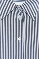 Camisa de algodón a rayas verticales azules y blancas, con cuello solapa y mangas cortas abullonadas. Cierre frontal con botones.