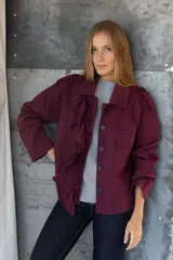 Chaqueta color bordó con cuello camisero, manga 3/4 y cierre frontal con botones negros. Presenta detalle de volantes en el frente y bolsillos de parche.