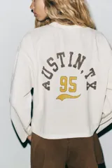 Sudadera blanca de algodón con cuello redondo y mangas largas. Estampado frontal con texto "Texas Rodeo 1995 United States" en color marrón.