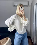 Blusa blanca de mangas largas con volados en los puños y escote con lazo.