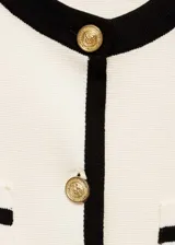 Cárdigan negro de punto fino con cuello redondo y manga corta. Presenta cierre frontal con botones dorados, ribetes blancos en contraste y dos bolsillos de ribete delanteros.